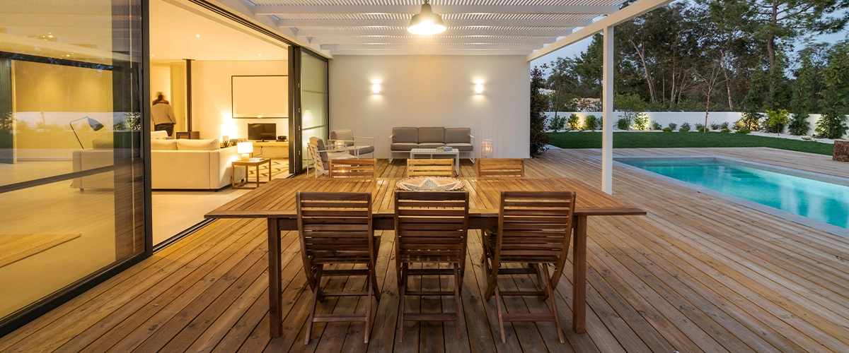 A wooden deck with a large table near a pool