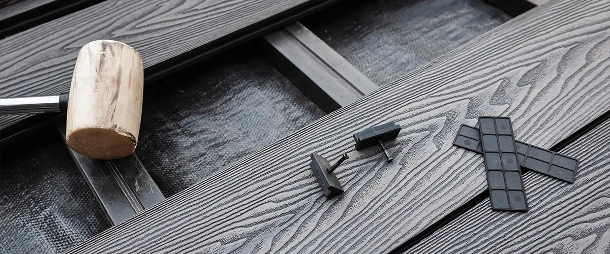 A black composite decking being installed with a wood mallet