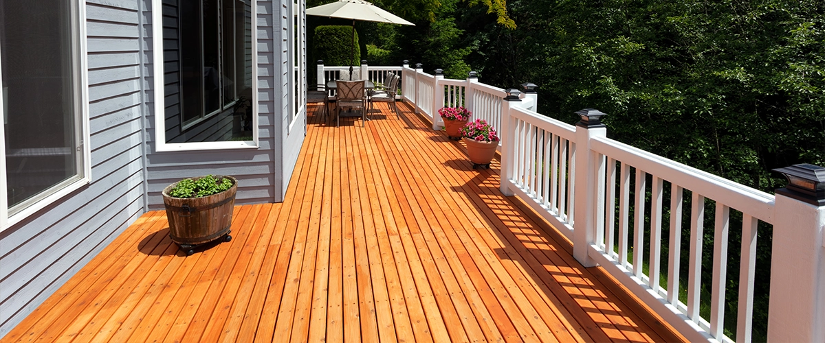 A cedar decking with white railing and gray home siding
