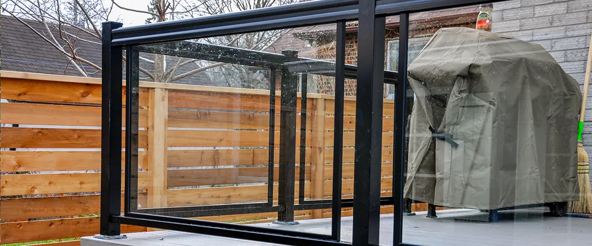 Metal railings with glass panels and a wooden fence in the background