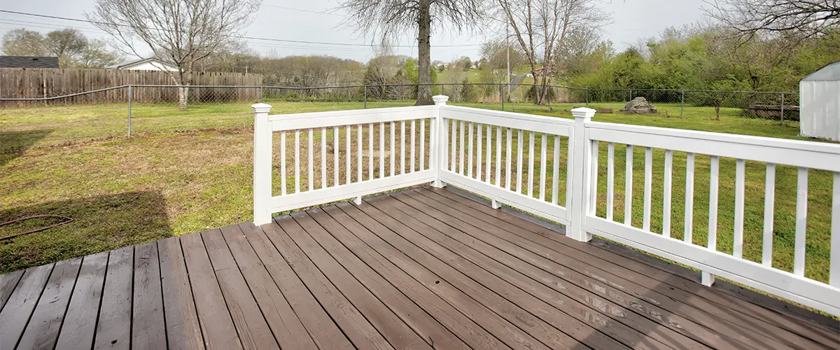 A wood deck stained with white railings in a backyard