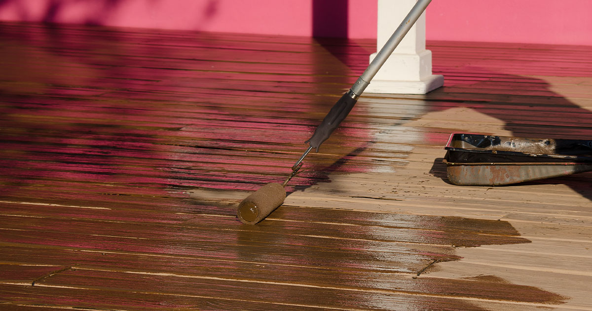 Man applying stain on wooden deck with roller illustrating Spraying Deck Stain Vs Rolling technique.