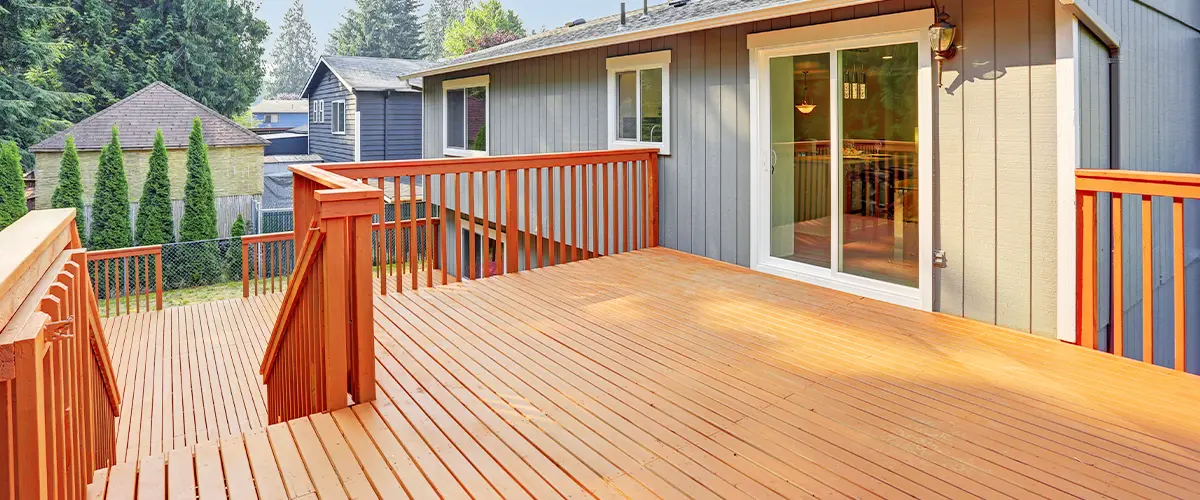 Spacious wooden deck attached to a suburban house, surrounded by trees and neighboring homes on a clear day