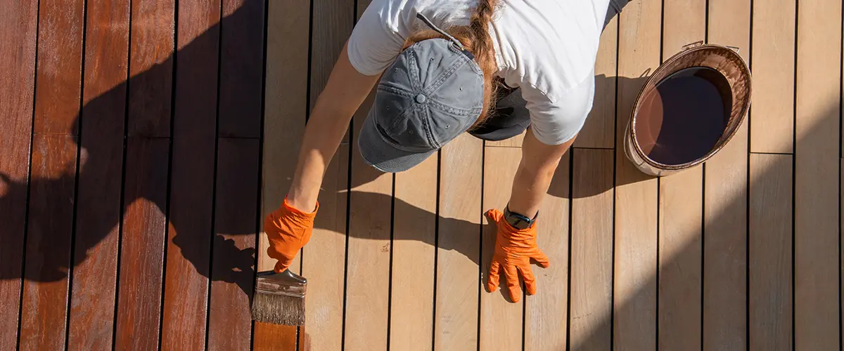 Worker staining a wood deck with a dark brown finish during home improvement project.