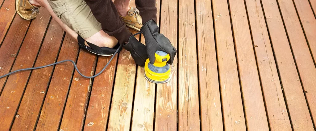 Man sanding wooden deck boards to refinish and prepare surface for staining. Staining And Refinishing Tips